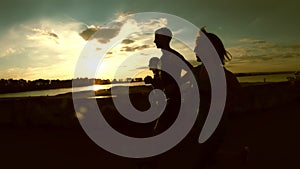 A group of athletes runners - two girls and a man running at city park, near river at sunset, silhouette, slow-motion