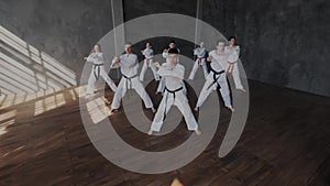 A group of athletes in white kimonos synchronously performs a set of taekwondo exercises. The combat school of the