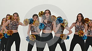 Group of athletic cheerleaders in silver tops and black tight leggings are dancing cheering dance on white studio