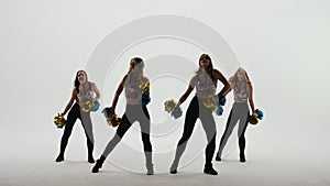 Group of athletic cheerleaders in silver tops and black tight leggings are dancing cheering dance on white studio