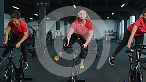 Group athletic girls performing aerobic riding training exercises on cycling stationary bike in gym