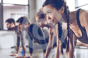 Group of athletic young people in sportswear doing push ups or plank at the gym