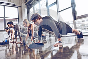 Group of athletic young people in sportswear doing push ups or plank at the gym