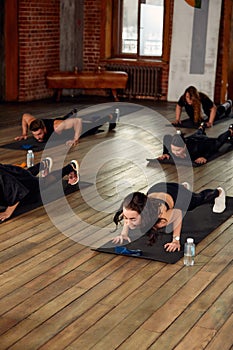 group of athletic young people in sportswear doing push ups or plank at the gym, group fitness concept