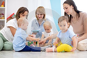 Group of babies and mothers playing with colorful educational toys in nursery room