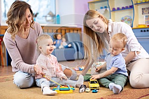 Group of babies toddlers playing with colorful educational toys and mothers in nursery room