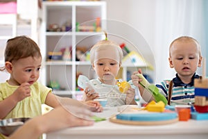 Group of babies is playing at table in nursery or creche. Toddlers in the day care center. Fun in the children`s