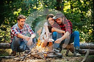 Group of backpackers relaxing near campfire. Friends spend leisure weekend forest nature background. Tourists relaxing