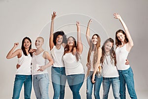 Group of beautiful diverse young women wearing white shirt and denim jeans having fun, looking cheerful while posing