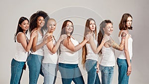 Group of beautiful diverse young women wearing white shirt and denim jeans looking at camera while posing, standing