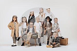 Group of beautiful kids, little girls and boys in modern outfits posing on grey studio background. Beauty, kids fashion