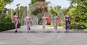 A group of beautiful women in tight-fitting tracksuits run along the path in the park