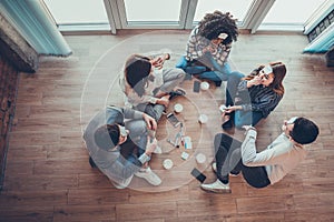 Group of beautiful young people sitting on floor in office having fun together playing name game with sticky notes to their