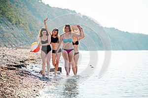 A group of beautiful young women in swimsuits cheerfully walk along the water along the seashore. Copy space. In the background,