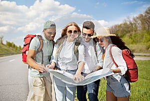 Group of best friends with backpacks checking map during road trip, hitchhiking on highway