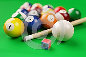 Group of billiard colored balls, cue and chalk on green table