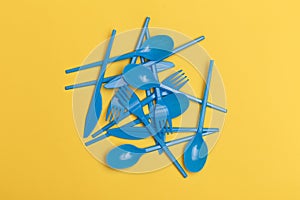 Group of blue disposable plastic knives, forks and spoons over a yellow background