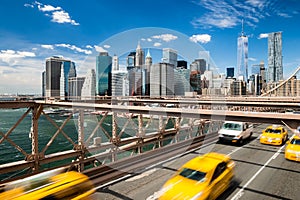 Group of blurred typical yellow New York cabs crossing the Brooklyn Bridge with the Manhattan skyline with blue sky with few cloud photo
