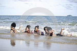 Group of boys and girls lie down in shallow sea water, cute kids having fun on sandy summer beach, happy childhood friend playing