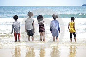 Group of boys standing in line in shallow sea water, cute kids having fun on sandy summer beach, happy childhood friend playing