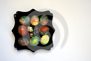 A group of brightly colored Easter eggs on a black curly plate on a white background