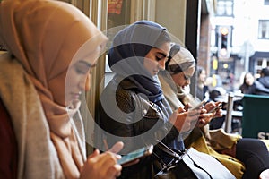 Group Of British Muslim Women Texting Outside Coffee Shop photo