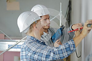 Group builders in hardhats with electric drill indoors