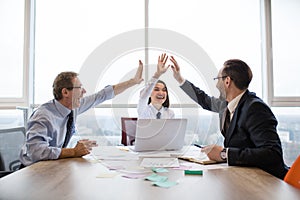 A group of business colleagues giving each other high-five and smiling while working in the officce