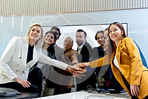 Group of business men and women join hands and look forward with smiling in coference or meeting room