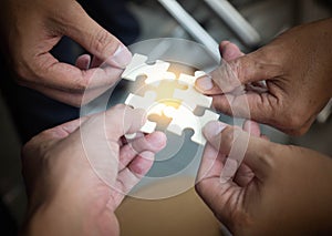 Group of business people assembling jigsaw puzzle wanting to put pieces of puzzle together on wood table backgroung for help suppo