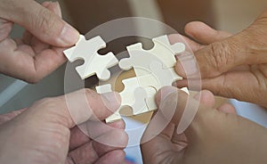 Group of business people assembling jigsaw puzzle wanting to put pieces of puzzle together on wood table backgroung for help suppo