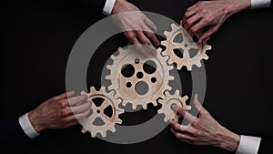 Group of business people connecting wooden cogwheels together on black background