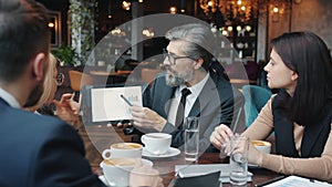 Group of business people discussing new project looking at tablet screen in cafe