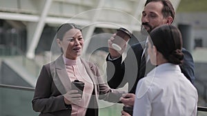Group of business people drink coffee on the street against the background of the business center. A man and two women