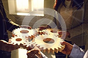 A group of business people holds wooden wheels with teeth in their hands on an office white table.