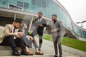 A group of business people meet outdoors. Male employees in suits communicate outdoors. Business partners discuss and