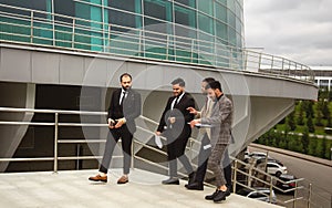 A group of business people meet outdoors. Male employees in suits communicate outdoors. Business partners discuss and