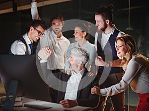 A group of business people in an office at night, expressing excitement.