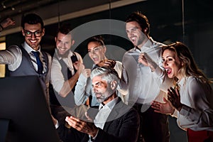 A group of business people in an office at night, expressing excitement.