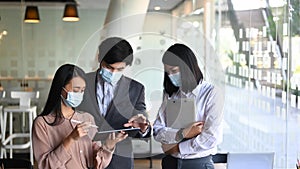 Group of business people in protective mask using digital tablet and discussing business strategy.