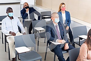 Group of business people in protective masks listening to presentation