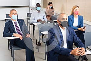 Group of business people in protective masks listening to presentation