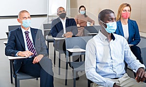 Group of business people in protective masks listening to presentation