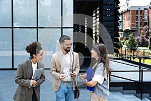 Group of business people walk outside in front of office buildings. Businessman and two businesswomen sharing experience ideas and