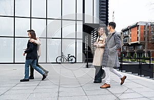 Group of business people walking outside in front of office building. Colleagues discussing on the way to the work. Young