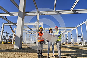 Group of Business People in Yellow and Red Hardhats Discuss a Project on Site Under Construction