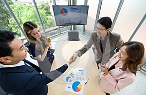 A group of business professional are in an office, engaging in a firm handshake following a successful meeting or agreement