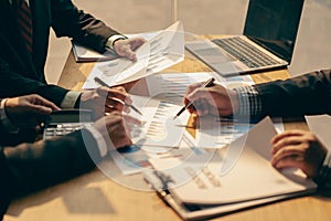 Group of businessmen holding smart pen discussing in group meeting at table in modern office with graph papers and laptop