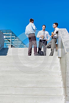 Group of businessmen standing and talking while drinking coffee during break