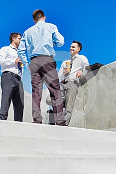 Group of businessmen standing and talking while drinking coffee during break